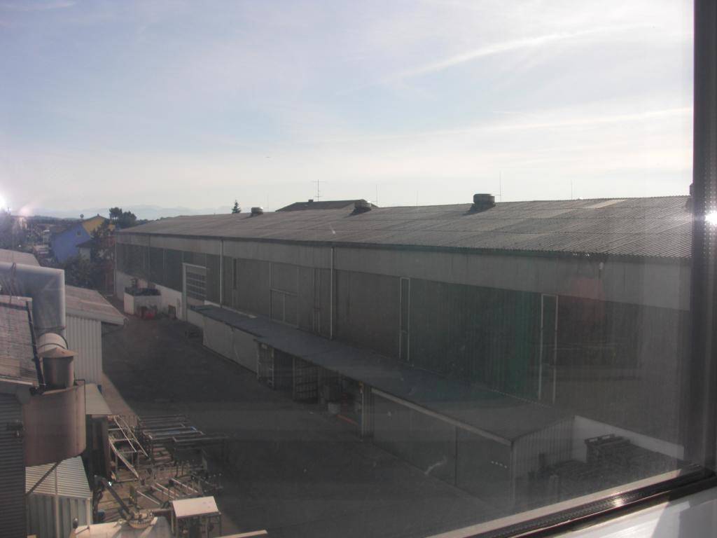 Blick aus einem Fenster auf die Rückseite eines großen Industriegebäudes mit Flachdach und Lagerflächen.
