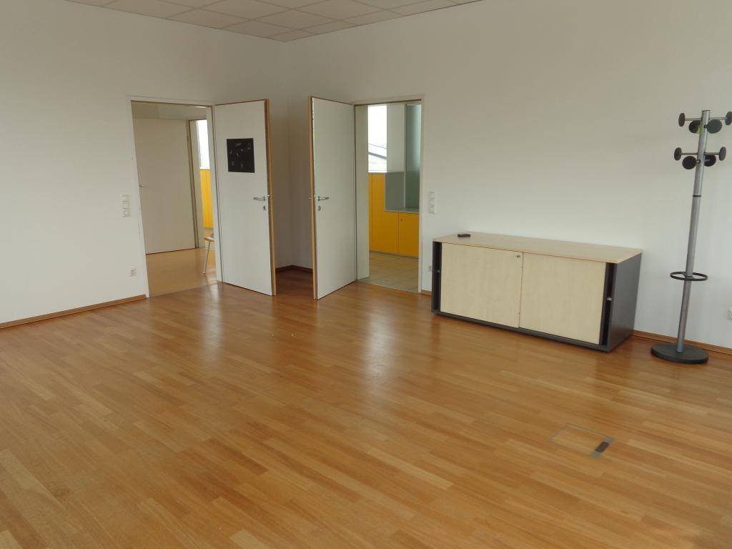 Leerer Büroraum mit Holzboden und zwei offenen Türen, die zu weiteren Räumen führen.