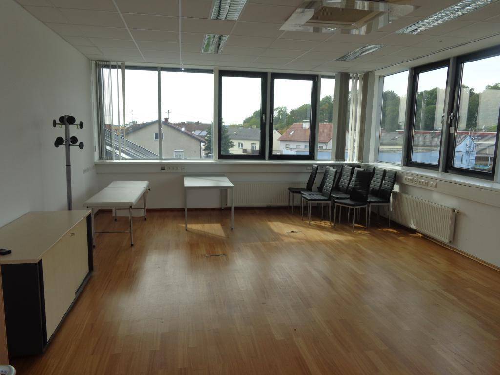 Helles, leeres Büro mit Holzfußboden, großen Fenstern und Blick auf die umliegende Bebauung.