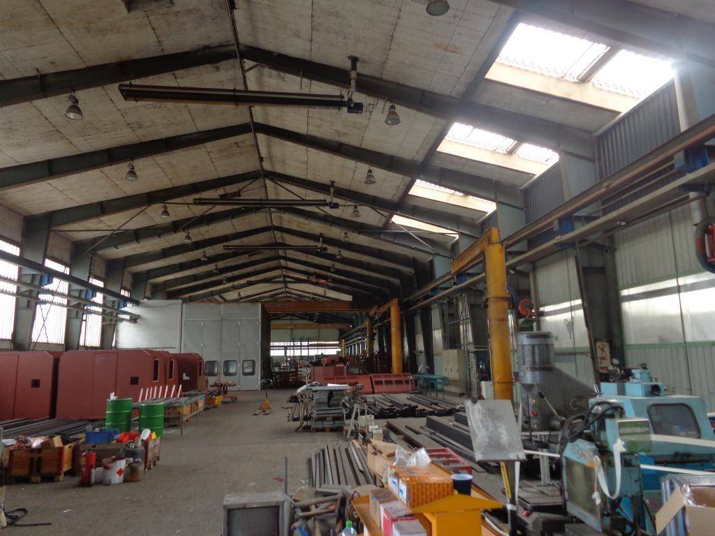 Große Industriehalle mit Oberlichtern, Stahlträgern und verschiedenen Maschinen und Materialien.