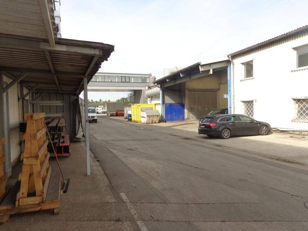 Zufahrtsweg zwischen mehreren Industriegebäuden mit geparkten Fahrzeugen und Lagercontainern.