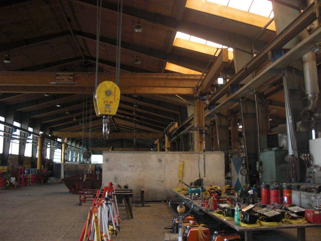 Große Lagerhalle mit hoher Decke, Oberlichtern und einem Kran, gefüllt mit Arbeitsmaterialien.