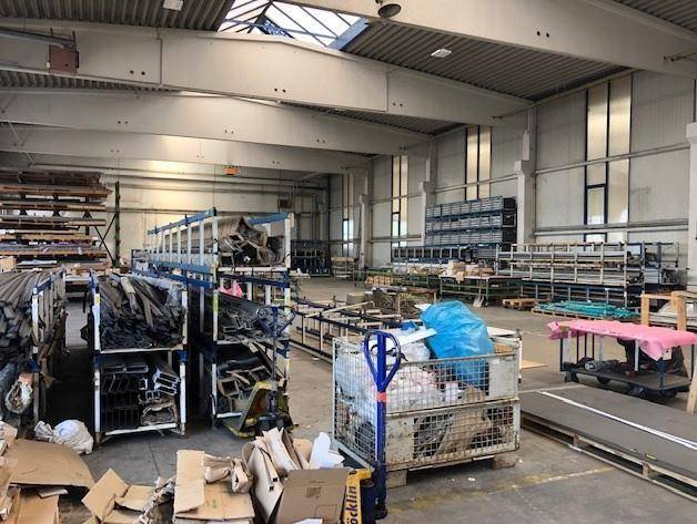 Große Lagerhalle mit Regalen voller Materialien, hohen Decken und natürlichem Lichteinfall.