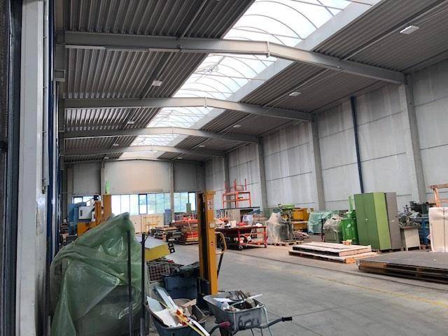 Geräumige Lagerhalle mit hohen Decken, Oberlichtern und verschiedenen Arbeitsgeräten.