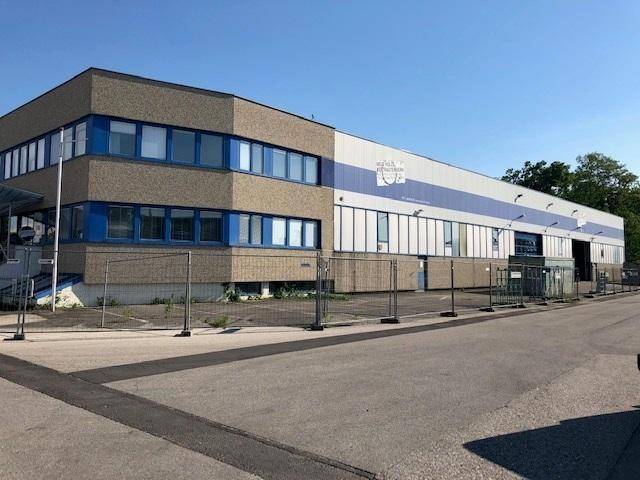 Weitläufige Ansicht des Gewerbegebäudes mit Bürotrakt und Lagerhalle unter blauem Himmel.