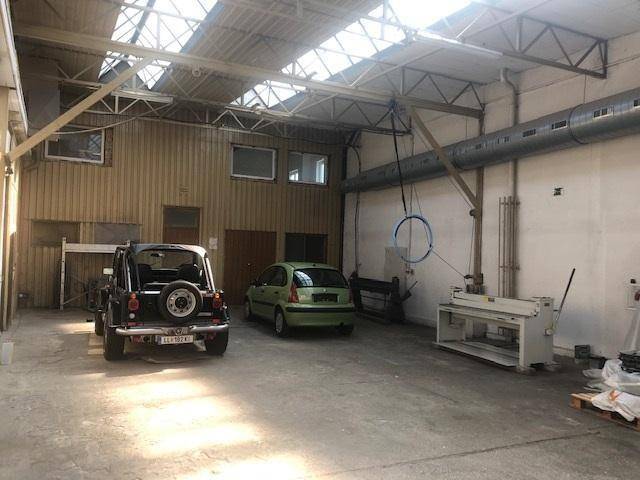 Große Lagerhalle mit zwei geparkten Autos, sichtbaren Dachbalken und Oberlichtern für Tageslicht.