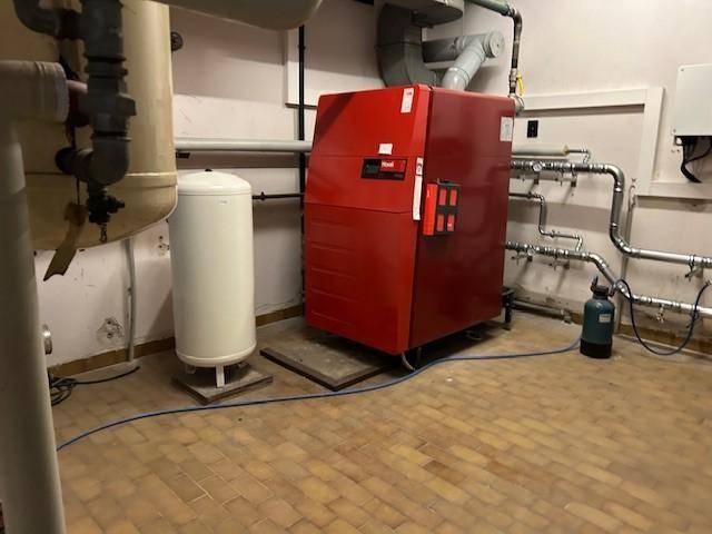 Heizungsraum mit einem großen roten Heizkessel, Rohren und einem Warmwasserspeicher.