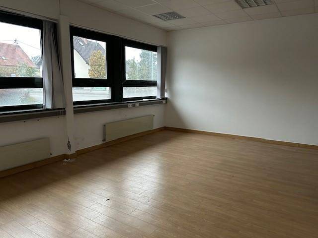 Heller Büroraum mit großen Fenstern, Laminatboden und Heizkörpern an den Wänden.