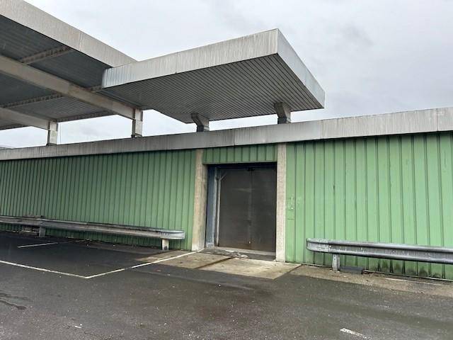 Grüne Wellblechfassade eines Gebäudes mit großer Tür und einem schützenden Vordach.