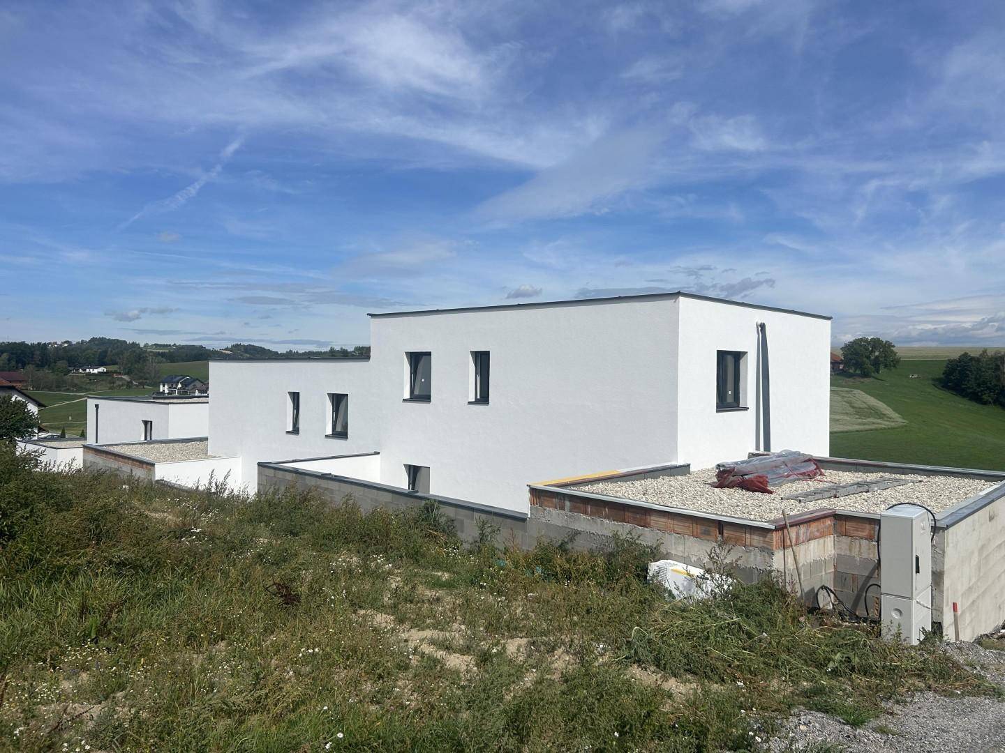 Mehrere moderne Neubauten mit Flachdächern in ländlicher Umgebung unter blauem Himmel.