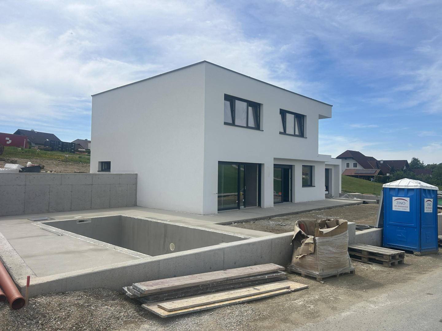 Neubau eines modernen Hauses mit Flachdach und einer im Bau befindlichen Poolanlage im Außenbereich.