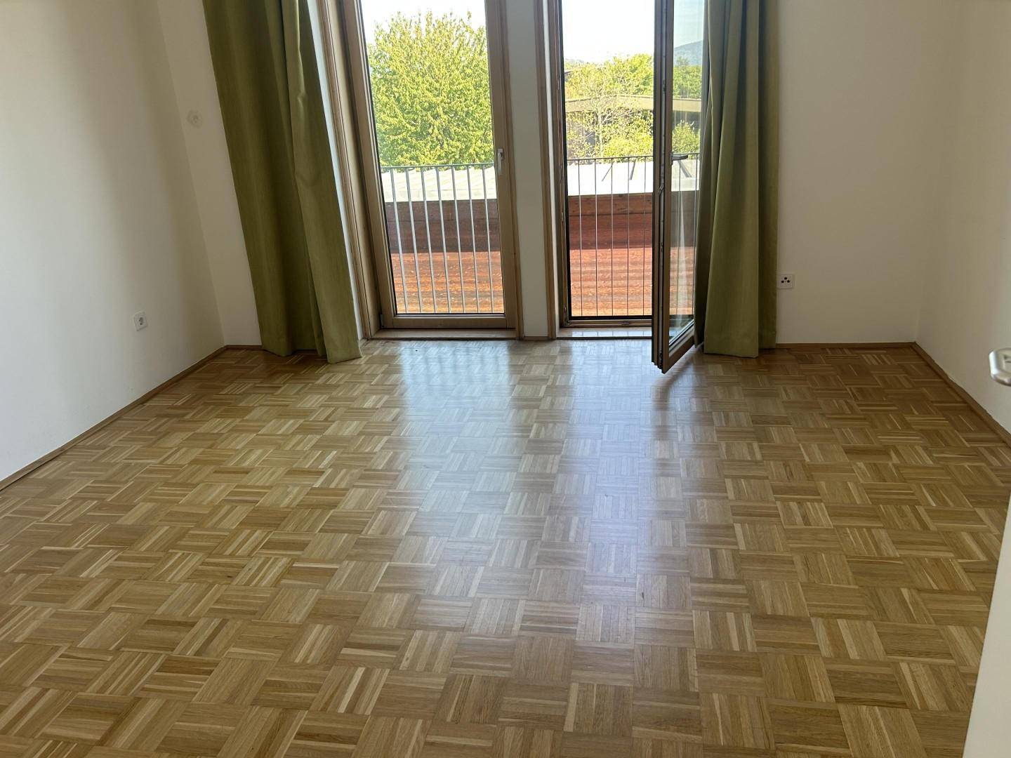 Geräumiges Zimmer mit Parkettboden und großen Fenstern zum Außenbereich.