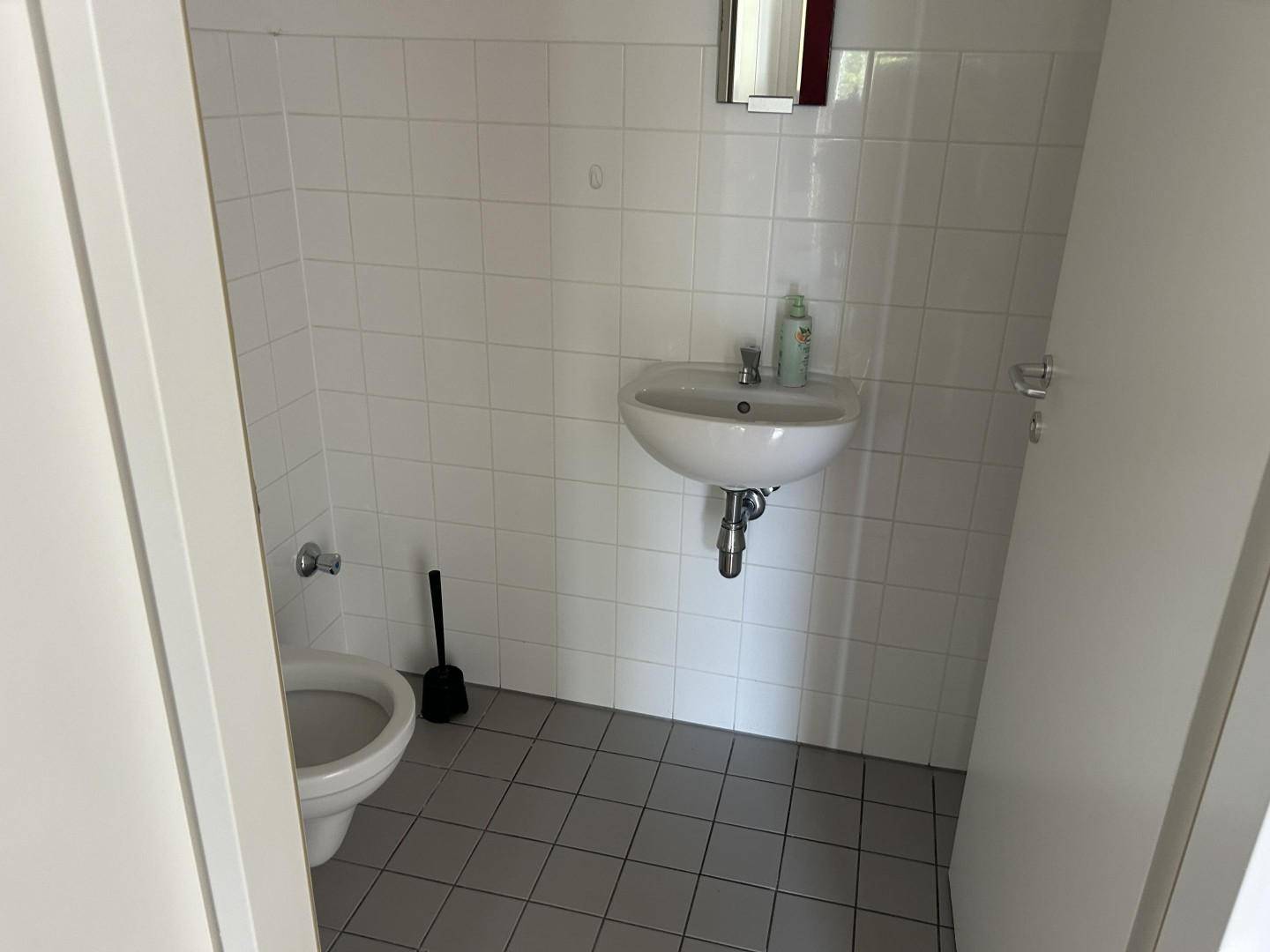 Kleines Gäste-WC mit weißen Fliesen, Toilette und Waschbecken.