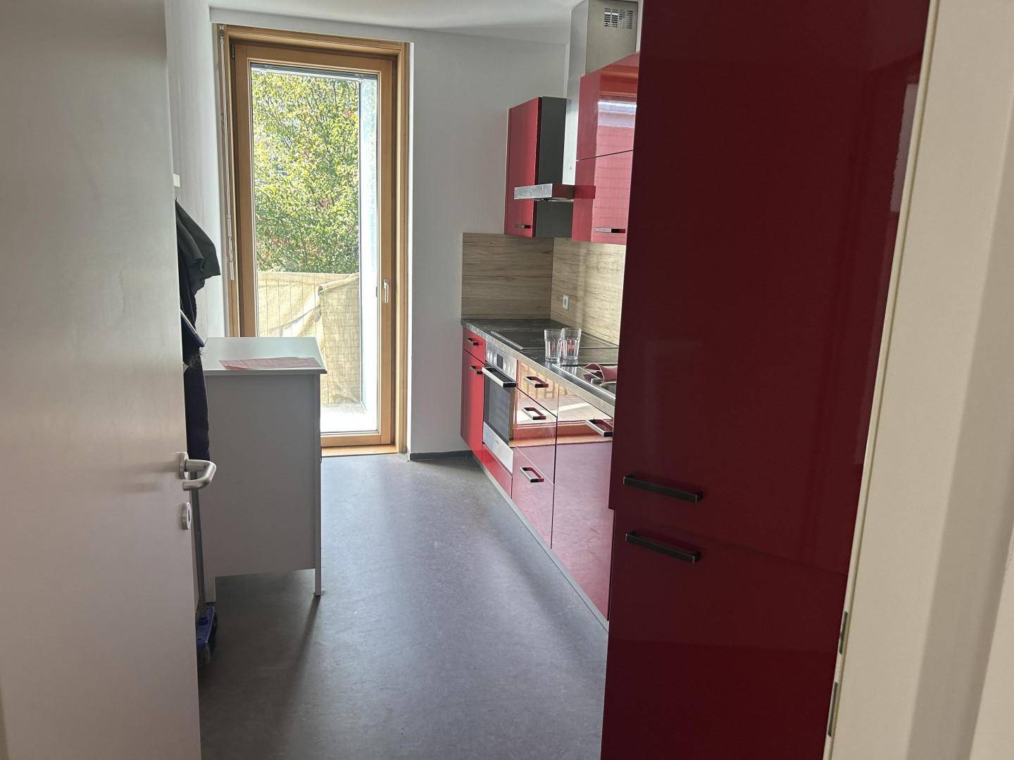 Moderne Küche mit roten Hochglanzschränken und Zugang zum Außenbereich.