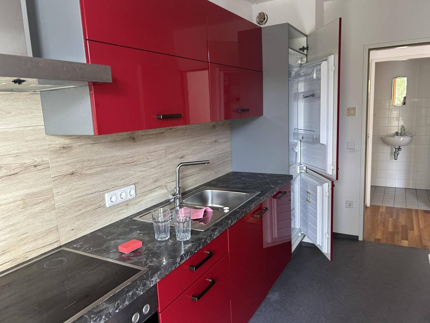 Funktionale Küche mit roten Schränken, Spüle, Kochfeld und Kühlschrank.