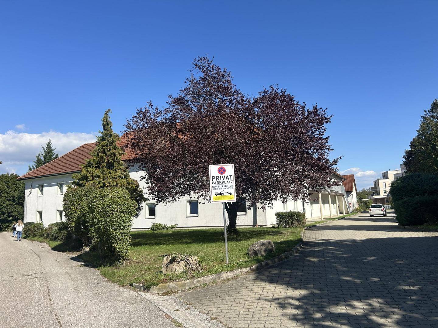 Außenansicht des Gebäudes mit einem Privatparkplatzschild und einem Baum mit roten Blättern.