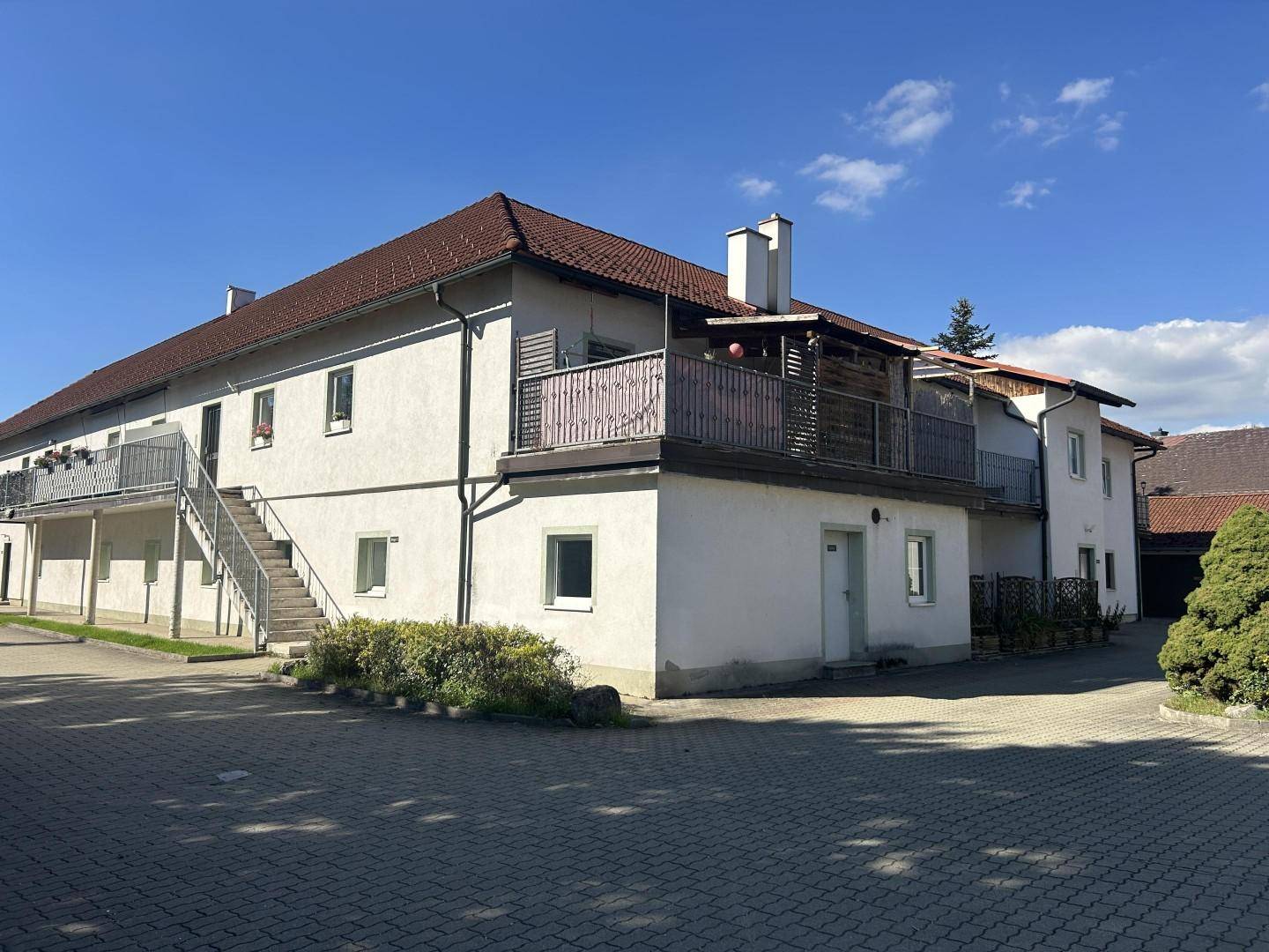Seitenansicht des weißen Gebäudes mit mehreren Balkonen und einer Außentreppe bei Sonnenschein.