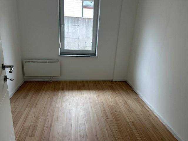 Leerer Raum mit Holzboden, weißen Wänden, einem Fenster und einem Wandheizkörper.
