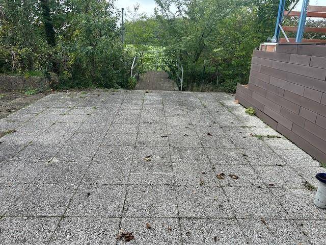 Gepflasterte Terrasse mit Blick auf eine grüne Fläche und Bäume im Hintergrund.