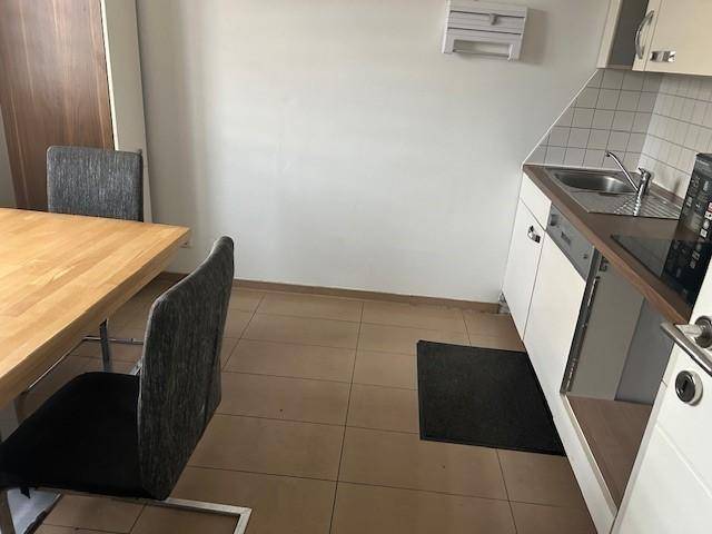 Kleine Küche mit Holztisch, weißen Schränken, Spüle und Kochfeld auf gefliestem Boden.