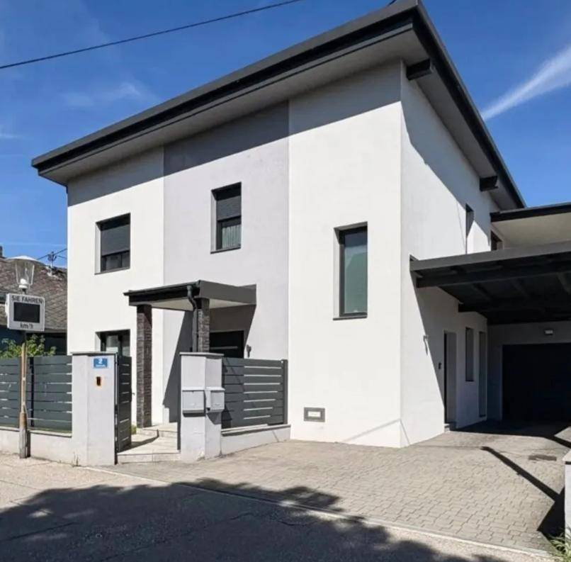 Moderne Hausfassade mit Carport und gepflegter Einfahrt unter strahlend blauem Himmel.