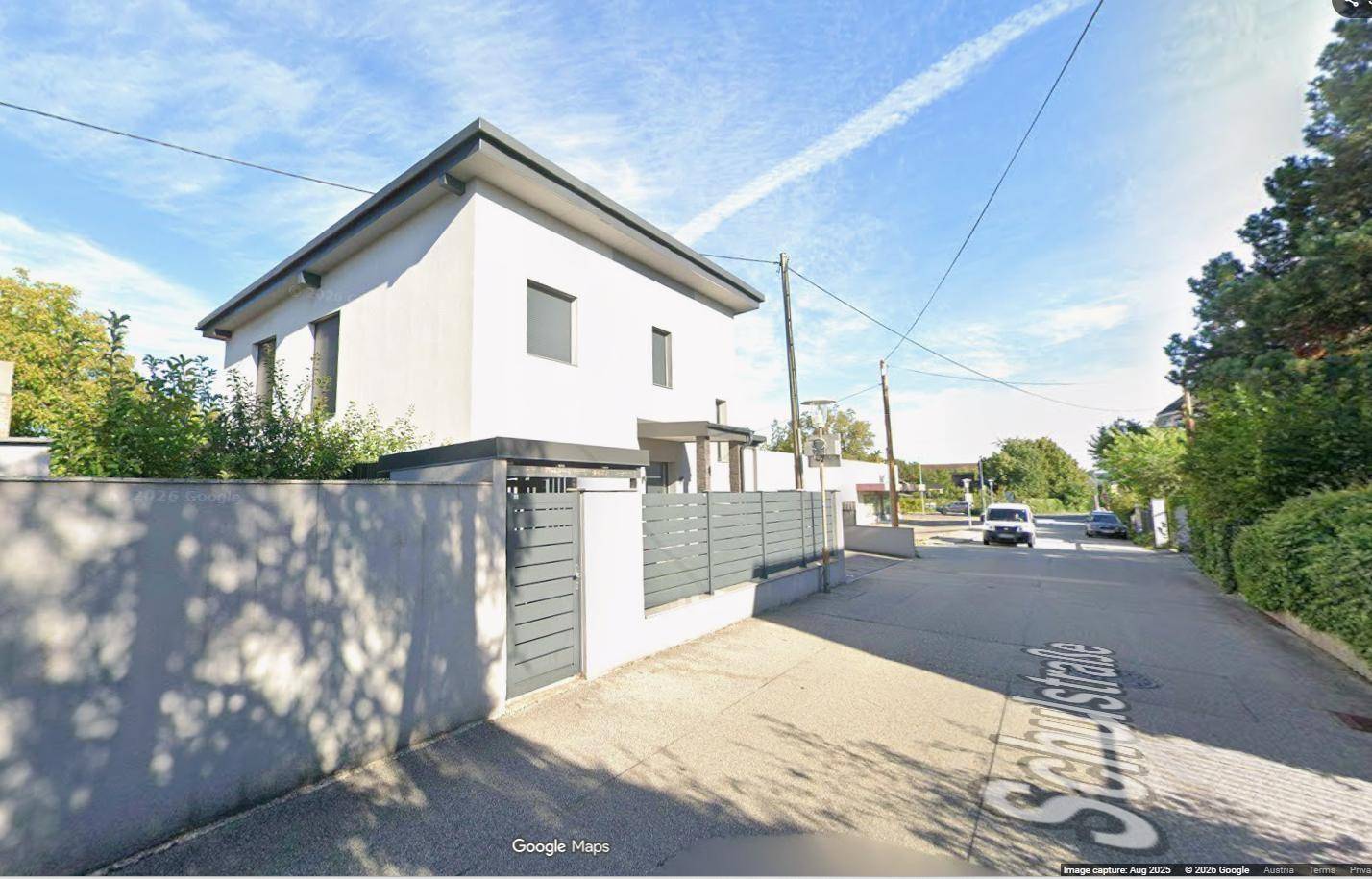 Das moderne Haus von der Schulstraße aus gesehen, umgeben von Grün und klarem Himmel.