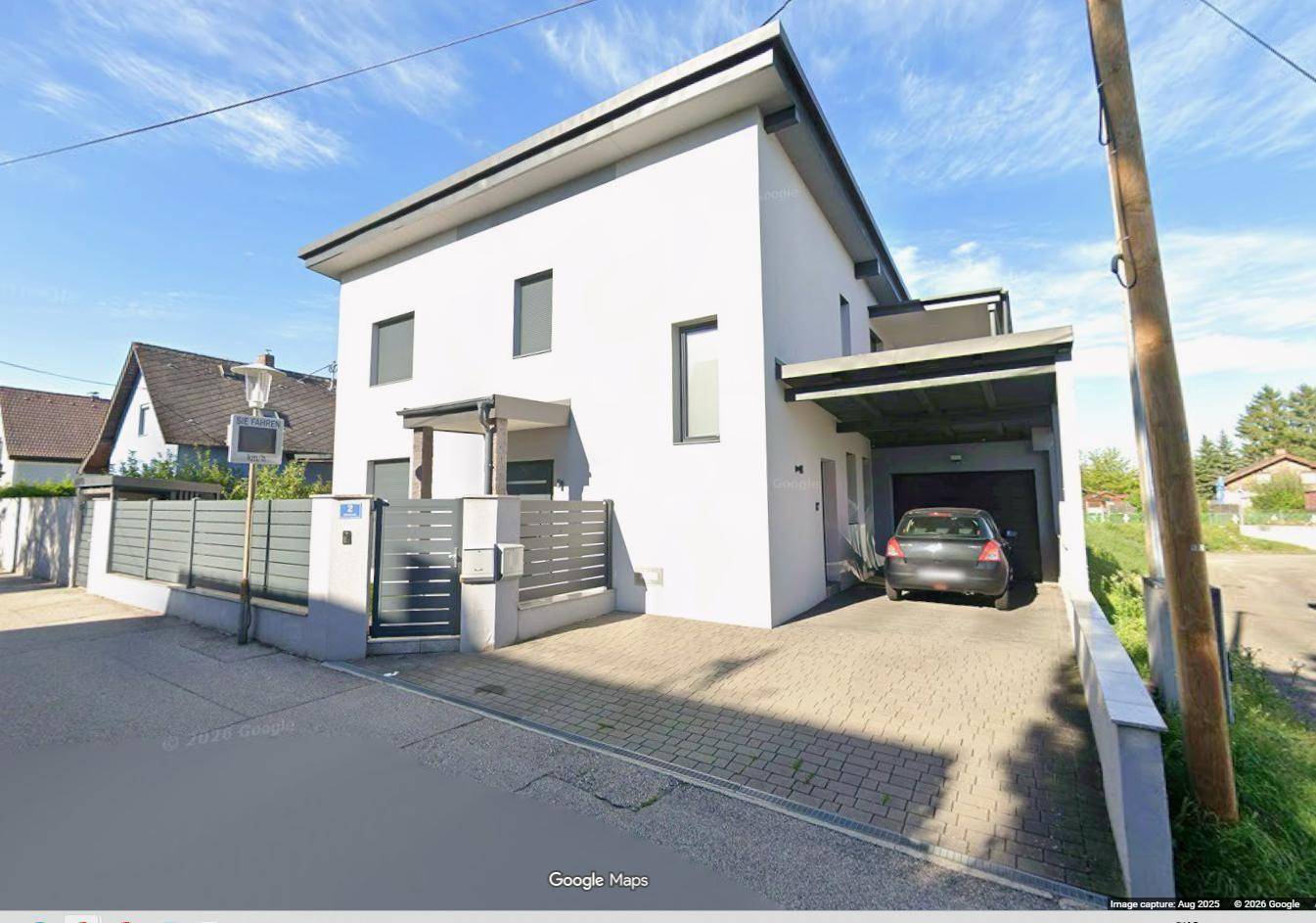 Ansicht des modernen Hauses von der Straße mit gepflasterter Einfahrt und Carport.
