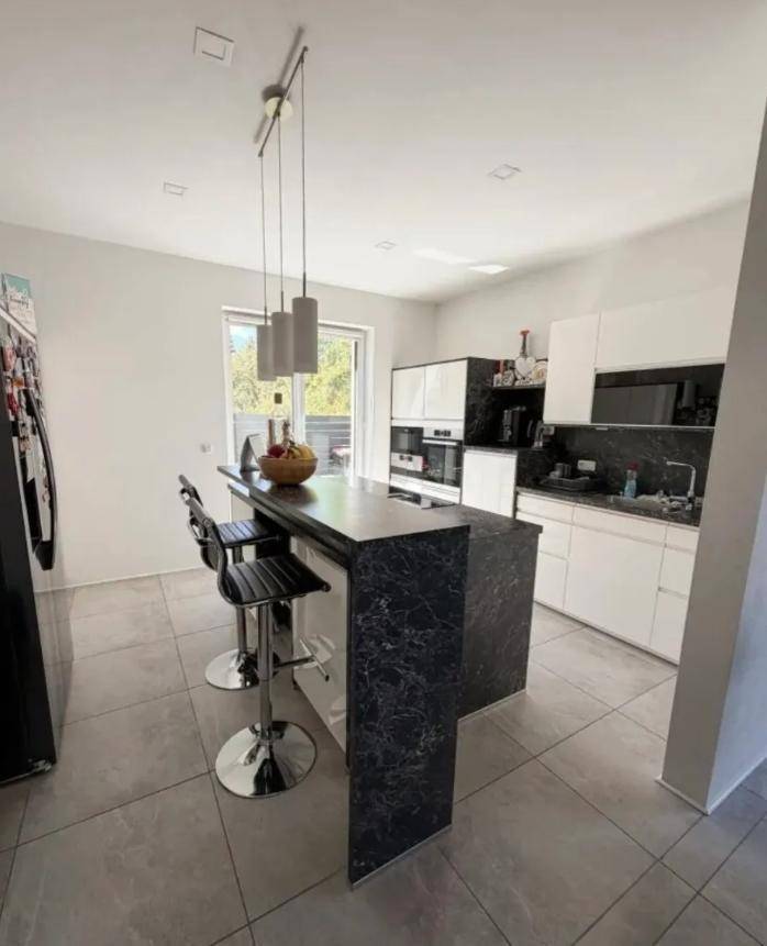 Moderne Küche mit Kochinsel, weißen Schränken und eleganten dunklen Arbeitsplatten.