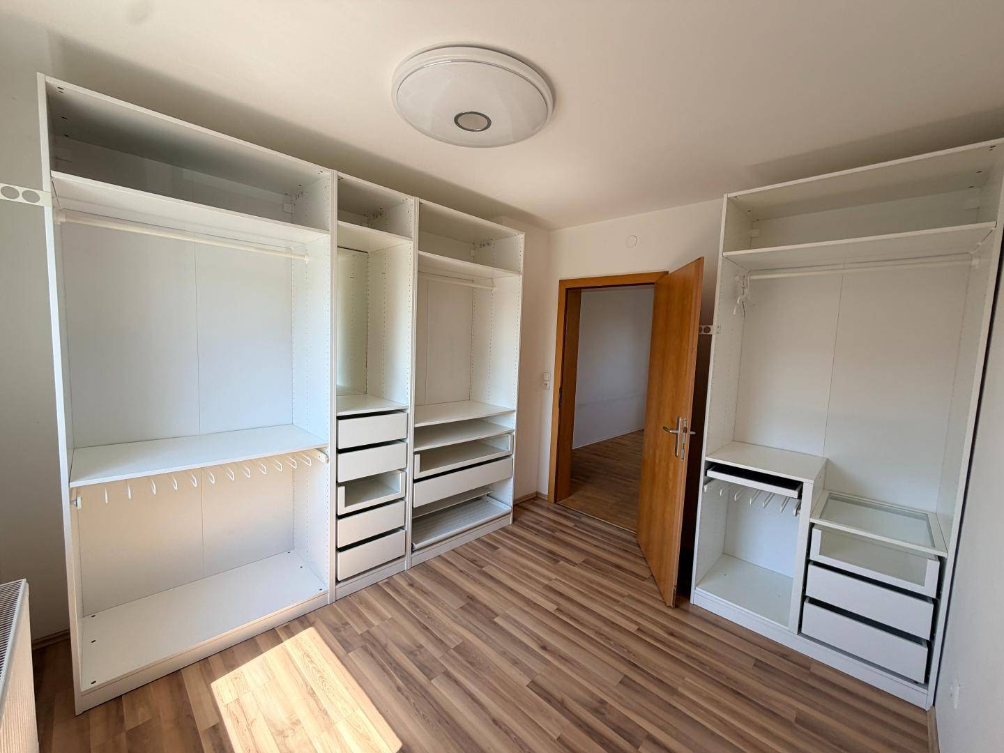 Schlafzimmer mit hellem Laminatboden und eingebauten weißen Kleiderschränken für viel Stauraum.