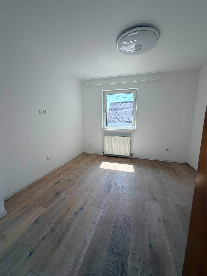 Helles Schlafzimmer mit modernem Laminatboden und einem Fenster, das viel Tageslicht hereinlässt.