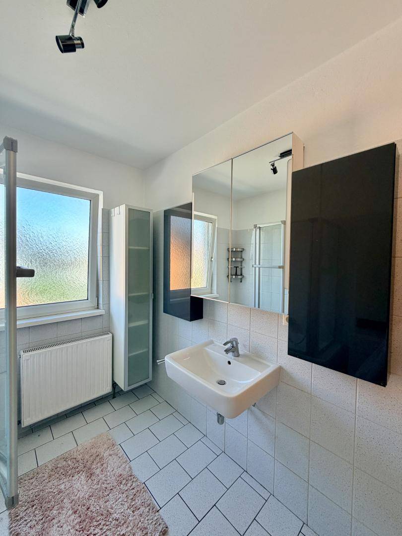 Modernes Badezimmer mit weißen Fliesen, Waschbecken und einem Spiegelschrank über dem Waschtisch.