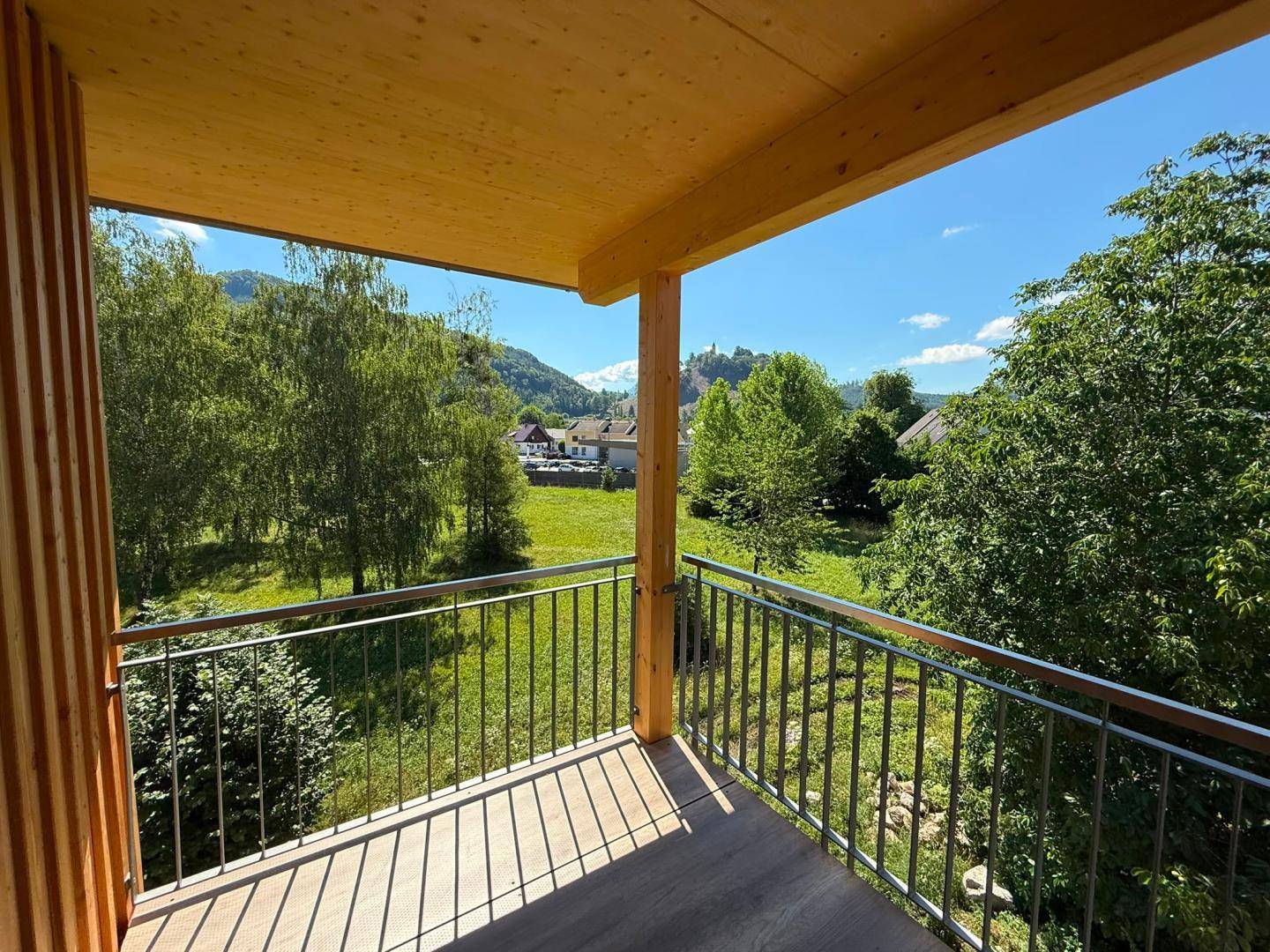 Balkon mit Holzbalkendecke und Blick auf grüne Landschaft und entfernte Gebäude.