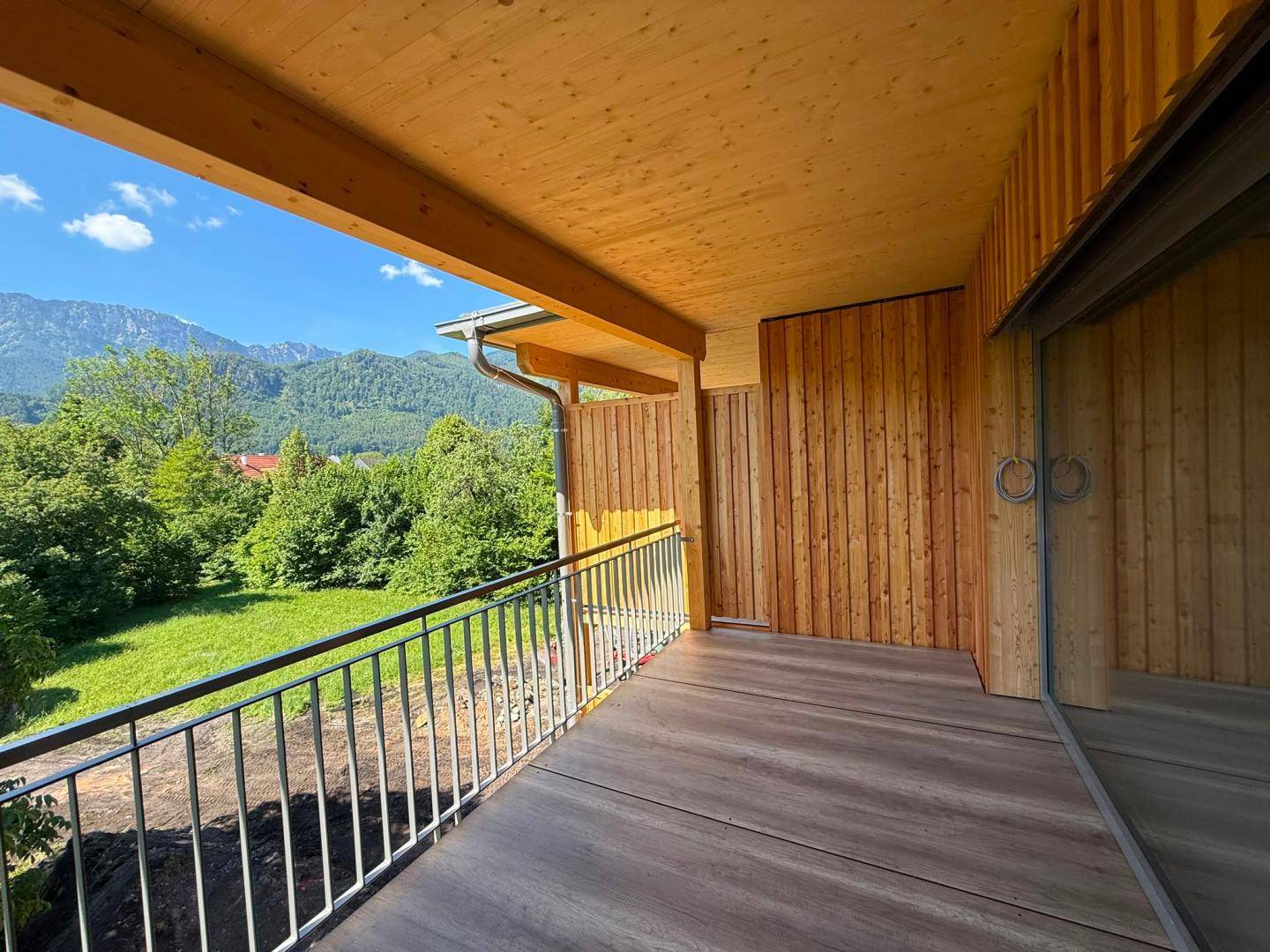 Heller Balkon mit Holzboden und Schiebetür, bietet einen weiten Blick auf die Berglandschaft.