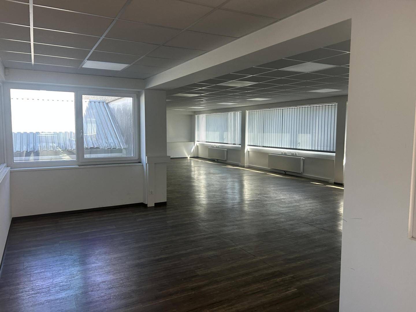 Großer, offener Bürobereich mit vielen Fenstern, Jalousien und einem dunklen Laminatboden, ideal für Großraumbüros.