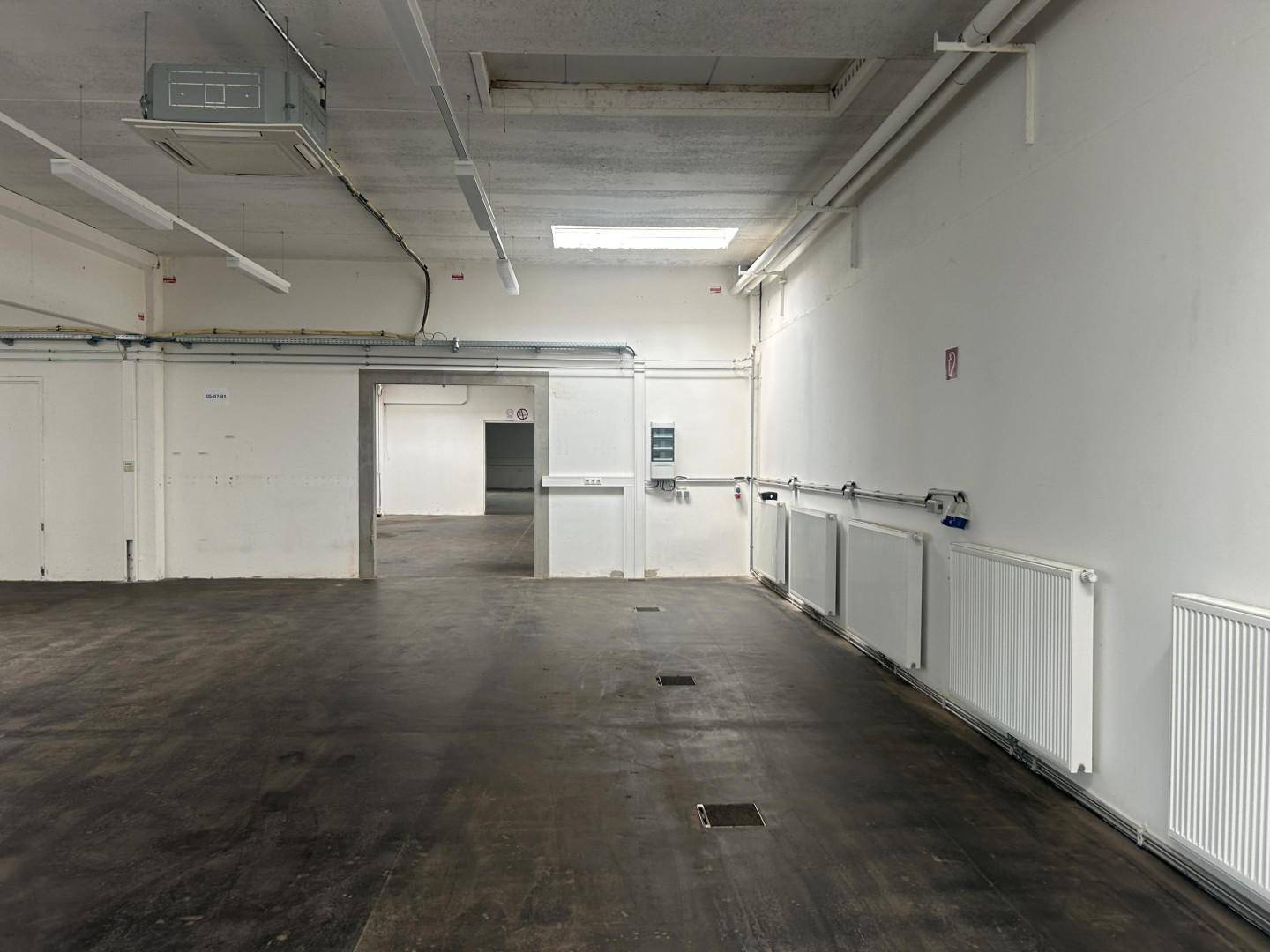 Geräumige Industriehalle mit Betonboden, Heizkörpern und sichtbaren Leitungen an den Wänden und Decken.