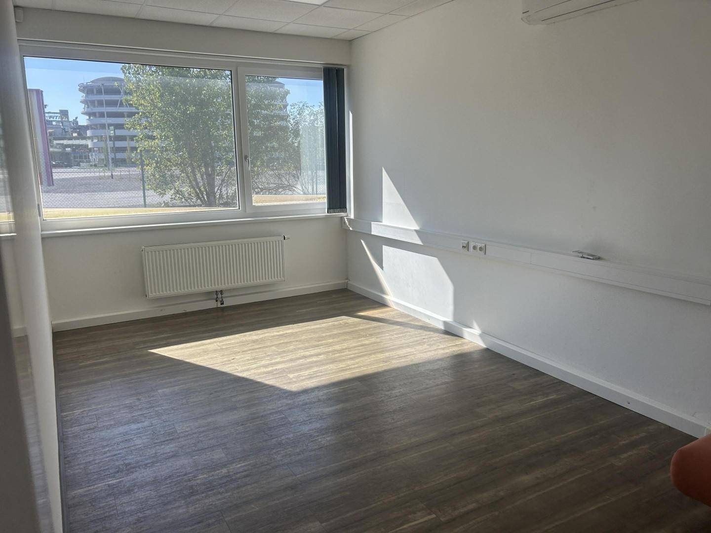 Heller Büroraum mit großen Fenstern, die einen Blick nach draußen bieten, und einem Heizkörper unter dem Fenster.