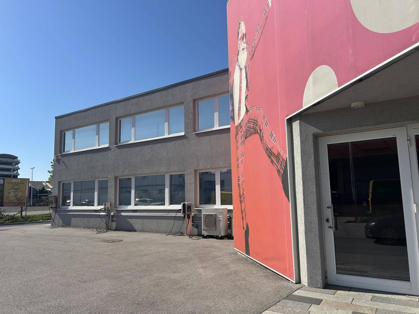 Modernes Geschäftsgebäude mit großen Fenstern und einer auffälligen roten Werbefläche an der Fassade.