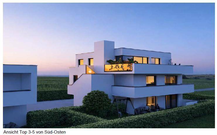 Moderne weiße Architektur bei Sonnenuntergang mit beleuchteten Innenräumen und grünen Hecken.