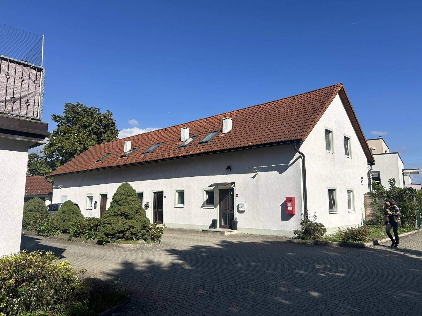 Längsseite des weißen Gebäudes mit mehreren Dachfenstern und roten Ziegeln unter blauem Himmel.
