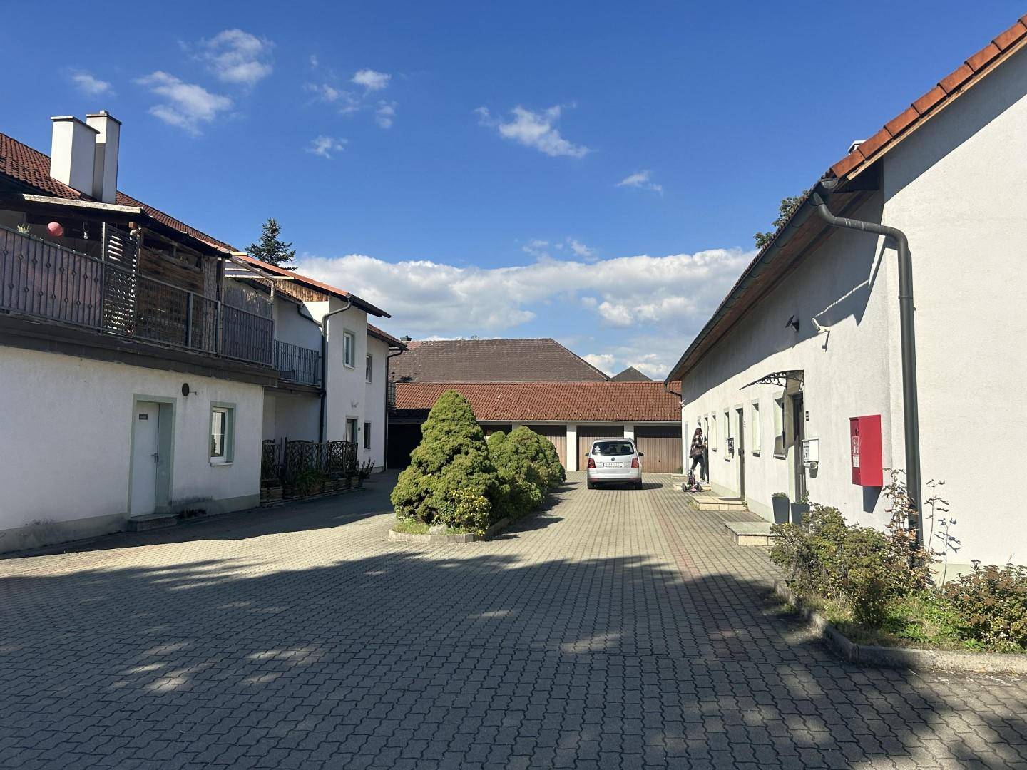 Gepflasterter Innenhof zwischen den Gebäuden mit einem geparkten Auto und Garagen im Hintergrund.