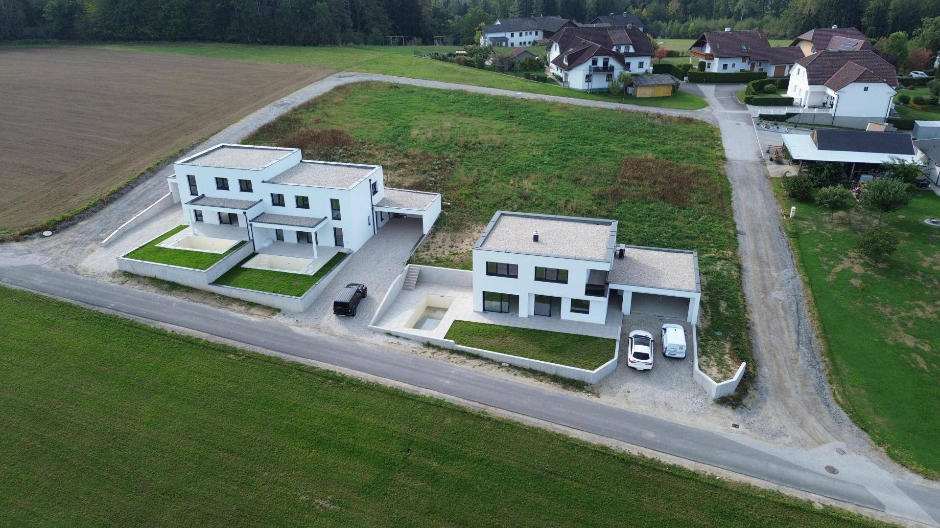 Luftaufnahme von zwei modernen weißen Häusern mit Flachdächern in einer weitläufigen grünen Landschaft.