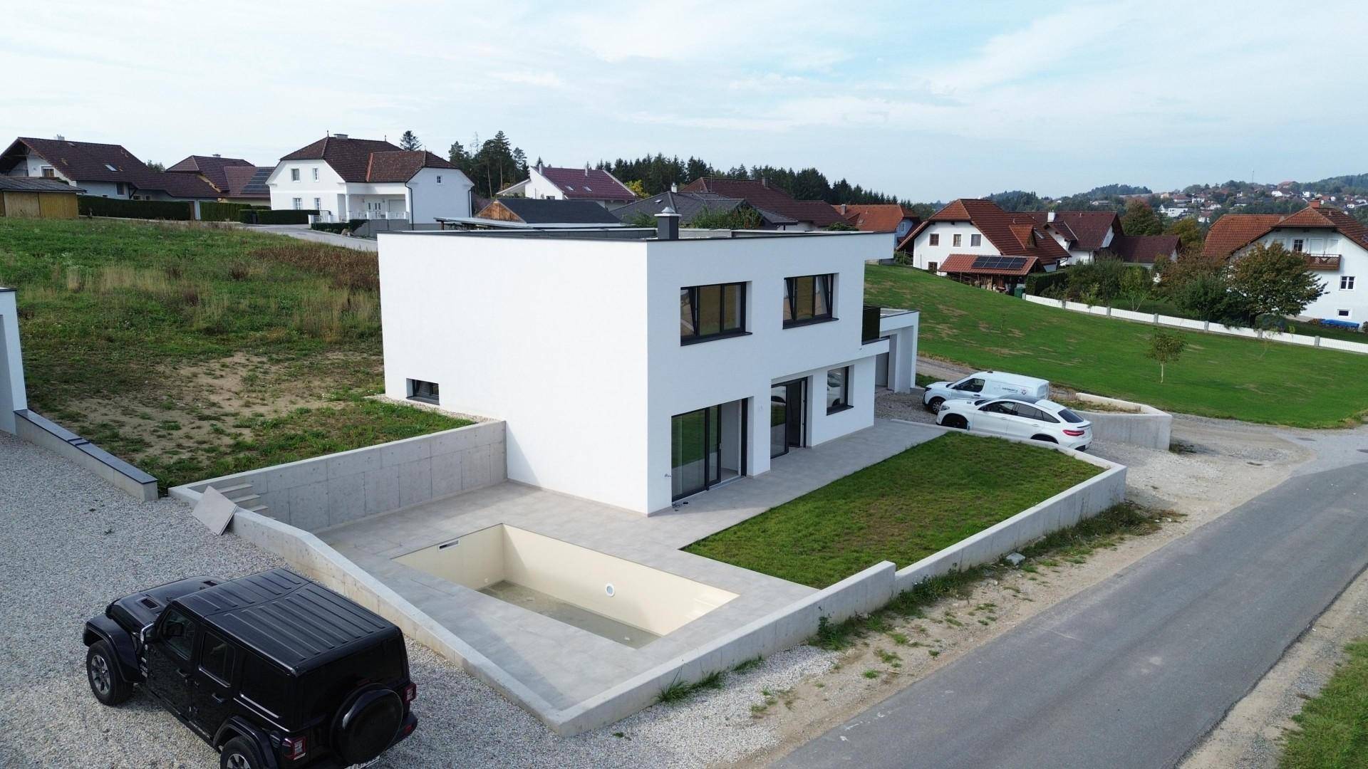 Modernes weißes Einfamilienhaus mit Flachdach, unfertigem Poolbereich und ländlicher Umgebung.