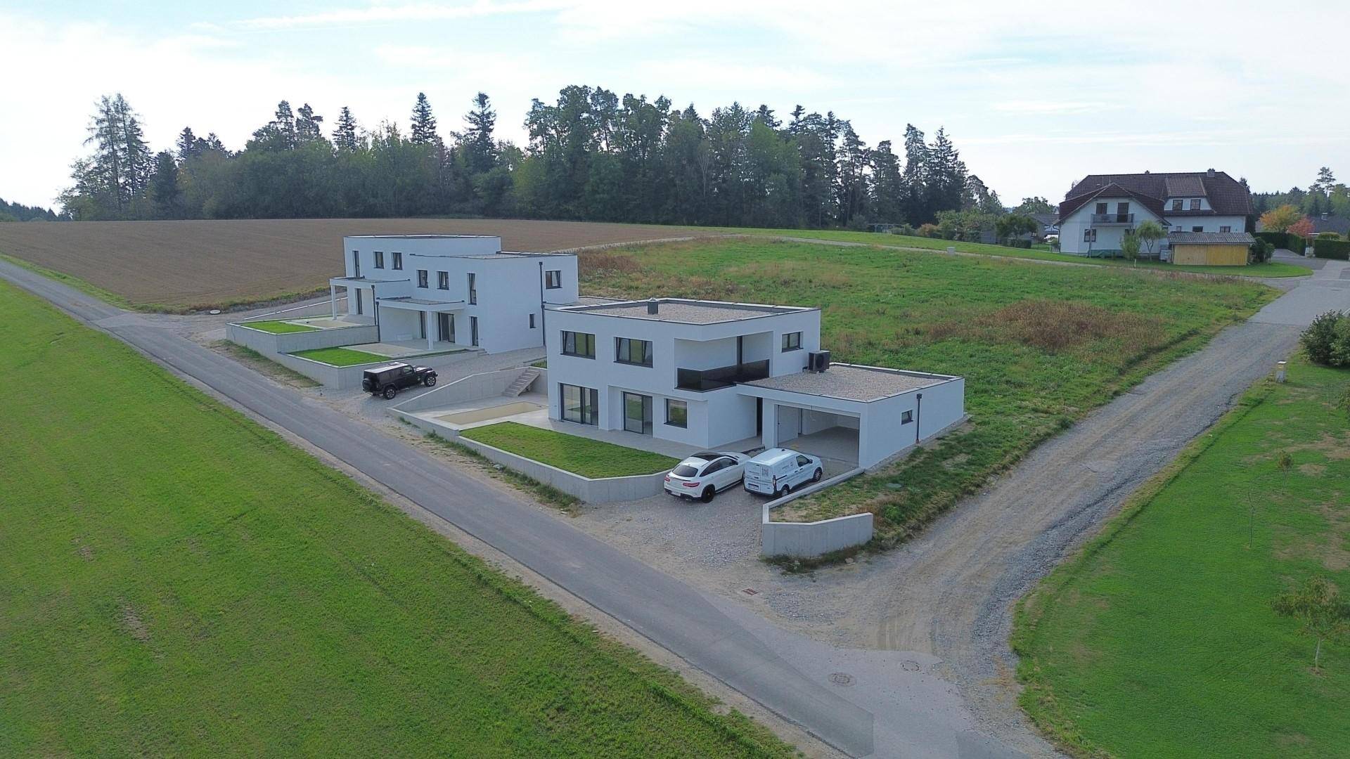 Weitläufige Luftaufnahme von zwei modernen Häusern mit Flachdächern in einer idyllischen ländlichen Umgebung.