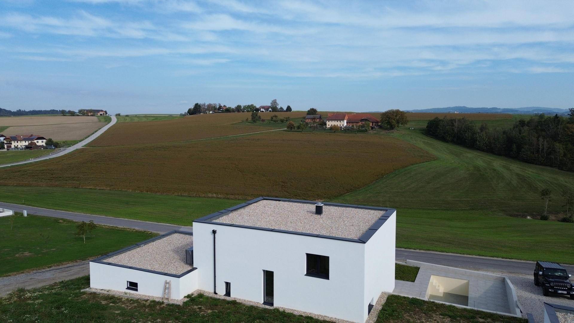 Rückansicht eines modernen Hauses mit Flachdach und Kiesbedeckung, umgeben von weiten Feldern.