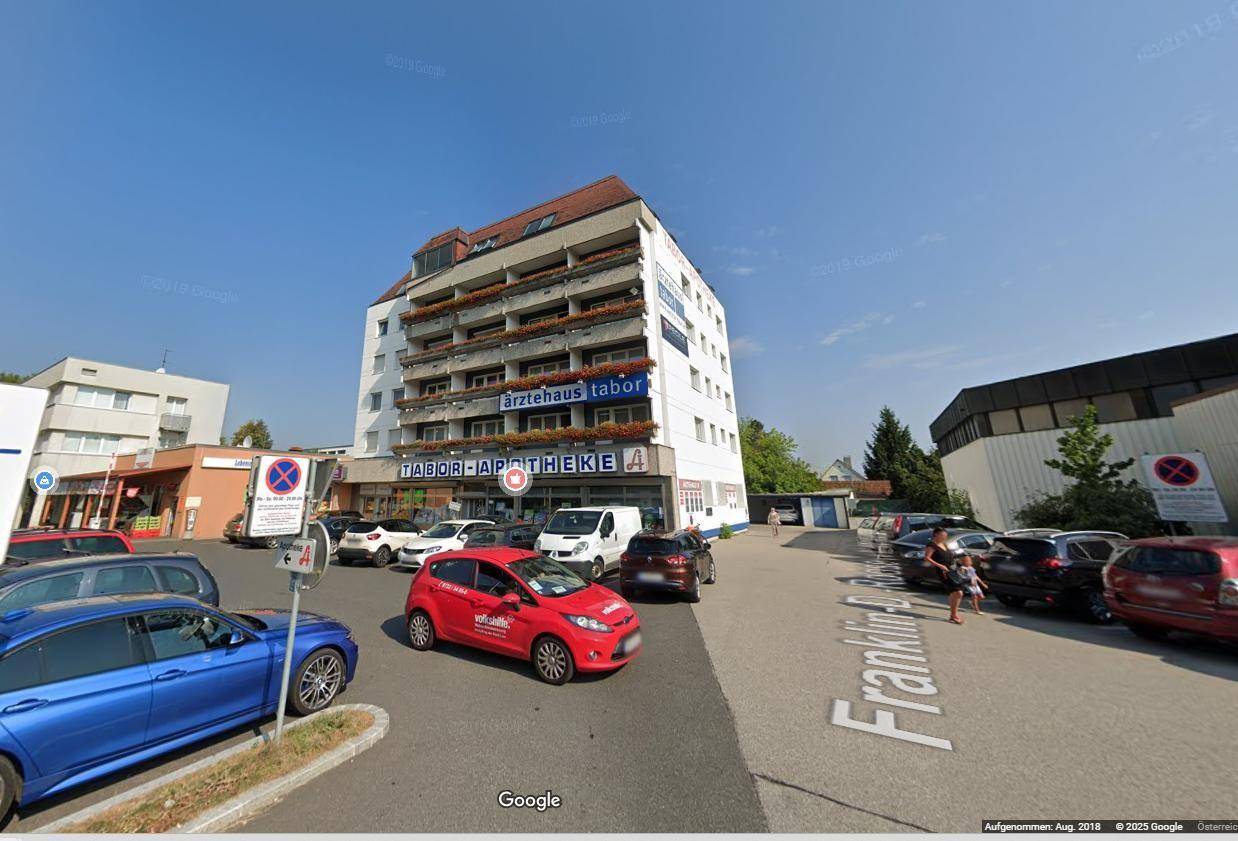 Weitwinkelansicht des Gebäudes mit umliegenden Straßen, vielen geparkten Autos und klarem Himmel.