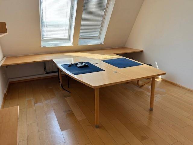 Büroraum im Dachgeschoss mit schrägen Wänden, zwei Dachfenstern und einem großen Holztisch.