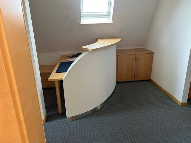 Empfangsbereich im Dachgeschoss mit Teppichboden, einem Dachfenster und einem geschwungenen Empfangstresen.