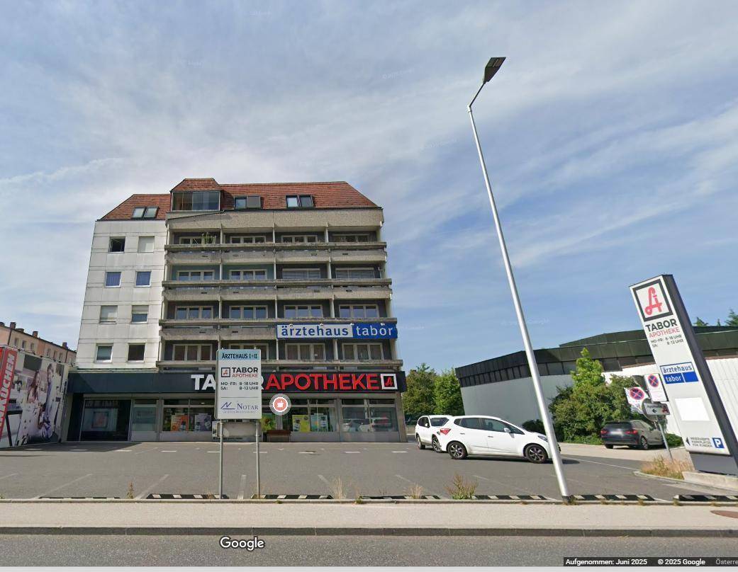 Ansicht des mehrstöckigen Gebäudes mit Parkplätzen davor und einer Straßenlaterne im Vordergrund.