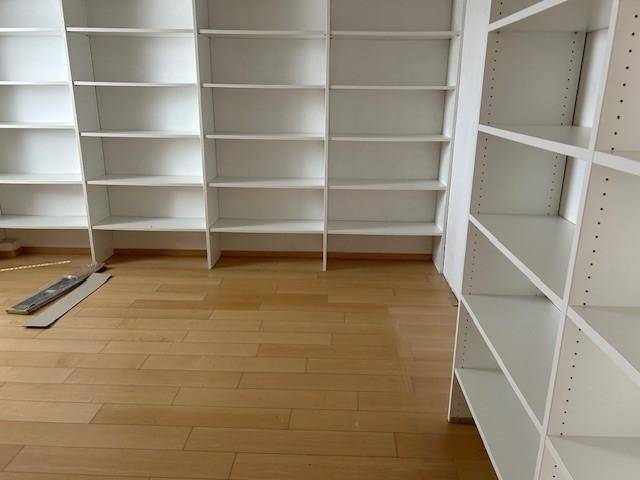 Heller Raum mit hellem Holzfußboden und mehreren weißen, leeren Bücherregalen entlang der Wände.