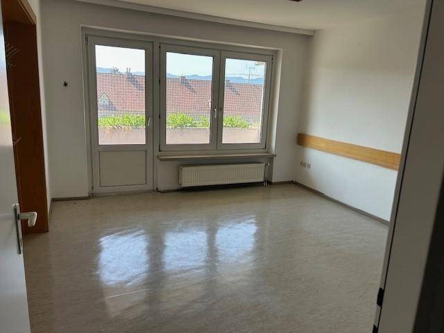 Heller Büroraum mit großen Fenstern, die auf Dächer blicken, und einem Zugang zu einem möglichen Balkon.